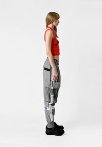 Pantalones cargo grises con múltiples bolsillos, acentos en blanco y azul, cintura elástica, combinados con una camiseta sin mangas roja ajustada y zapatos negros tipo slip-on.