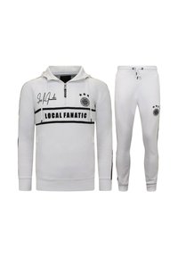 Wit trainingspak bestaande uit een pullover met een ritssluiting bij de hals en een broek. Voorzien van zwarte strepen, logo details en drie sterren op het bovenstuk.