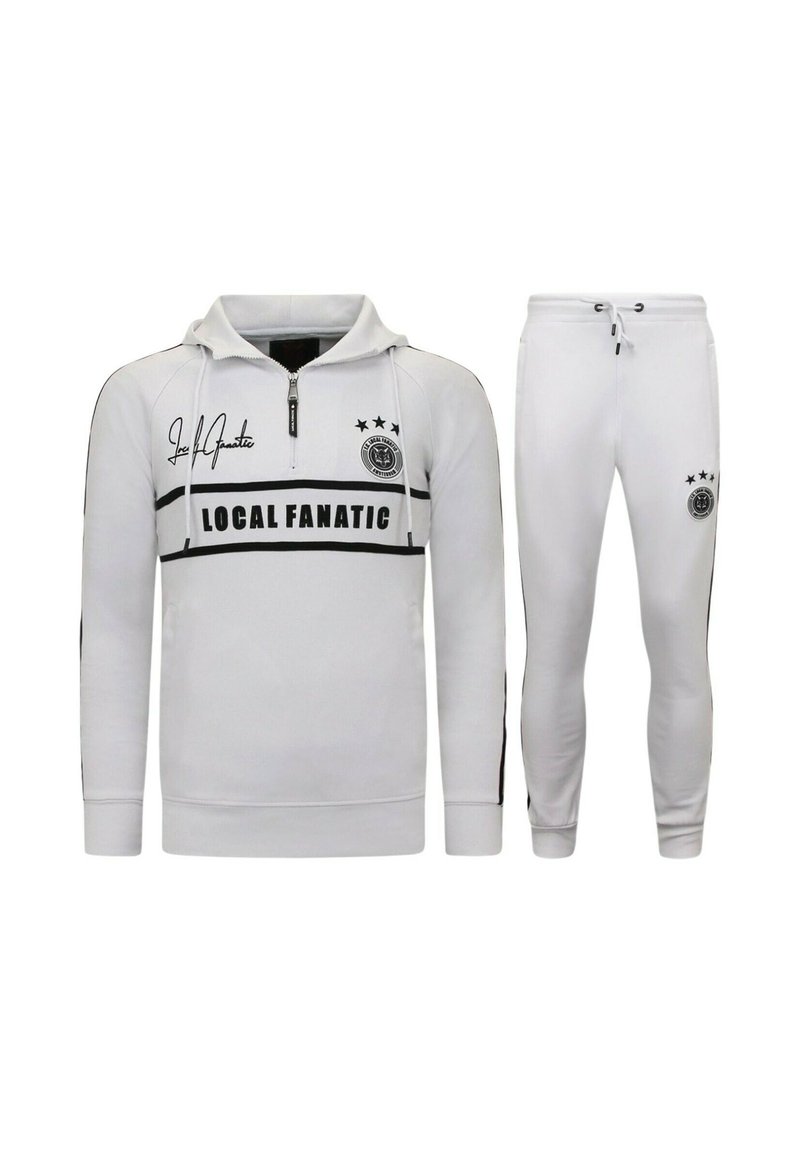 Wit trainingspak bestaande uit een pullover met een ritssluiting bij de hals en een broek. Voorzien van zwarte strepen, logo details en drie sterren op het bovenstuk.