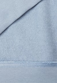 Textil azul claro con una textura tejida suave y un patrón acanalado, con costuras visibles a lo largo del borde.