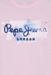 Camiseta rosa claro con un diseño gráfico azul que presenta el texto "Pepe Jeans" y "LONDRES" en una mezcla de fuentes manuscritas y en negrita.