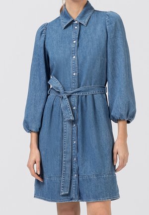 Denimskjole med puffede lange ærmer, knaplukning foran, spids krave og et bælte bundet i taljen.