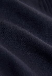 Gros plan d'un tissu bleu marine foncé avec des plis doux et une texture fine en maille visible en faible luminosité.