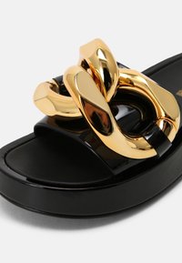 Sandale slide à plateforme noire avec un détail de grosse chaîne dorée brillante sur la bride supérieure.