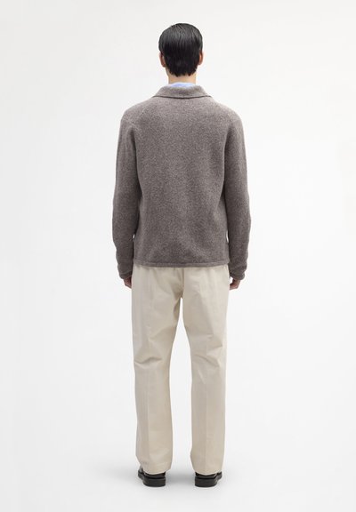 Cardigan en laine marron avec col châle, finition texturée et manches longues, associé à un pantalon de couleur crème et des chaussures noires.