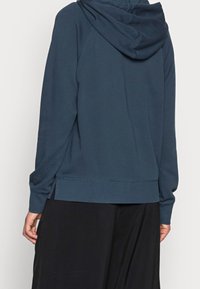 Sudadera azul oscura con una capucha amplia, mangas largas y aberturas laterales en el dobladillo; hecha de una suave tela texturizada.
