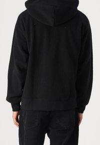 Svart hoodie tillverkad av strukturerad fleece, med en lös passform och ribbade muddar och nederkant. Enkel design utan synlig logotyp.