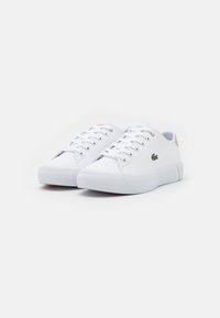 Hvite sneakers med en glatt tekstur, med lavt design, rund tå, snøring foran, og en liten grønn logo på siden.