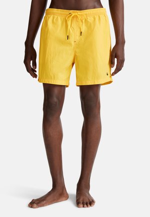 Gelbe Badehosen aus leichtem Material, mit einem elastischen Bund und Kordelzug sowie einer Länge über dem Knie.