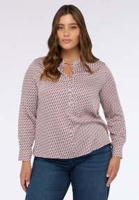 Blusa a maniche lunghe con base bianca e modelli geometrici rossi e blu, davanti con bottoni e dettaglio alla scollatura con occhiello e cordoncino.
