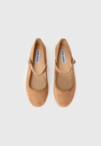 Pari loabeli beige suede Mary Jane datar dengan tali gesper, dilihat dari atas, di latar belakang putih.