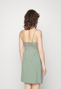 Hellgrünes Kleid mit dünnen Spaghetti-Trägern, das an der Rückseite ein kunstvolles besticktes Design aufweist und aus weichem, leichtem Material gefertigt ist.