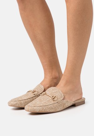 Mule in lino beige con finitura testurizzata, punta appuntita e un accento decorativo in hardware dorato. Tacco basso per un maggiore comfort.