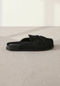 Sandale à semelle plate en daim noir avec des accents de franges, à design simple. Surface texturée avec des lignes épurées et un minimum de matériel.