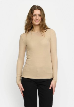 Beige pitkähihaisessa istuvassa paidassa on ribatut pinnat, pyöreä pääntie ja saumat, jotka on paritettu mustien housujen kanssa.