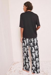 Cămașă neagră cu mâneci scurte, asociată cu pantaloni largi cu un print animalic alb pe un fundal negru. Textura materialului este netedă.
