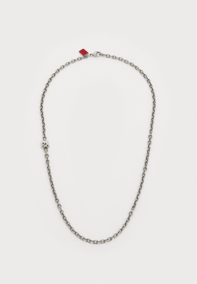 Ασημένια αλυσίδα κολιέ που διαθέτει επιμηκυμένα κεριά με διακοσμητικό στοιχείο, μια μικρή κόκκινη ετικέτα προσαρτημένη, λεία υφή και γυαλιστερή φινίρισμα.
