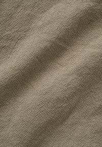 Tissu en lin marron clair froissé avec une texture tissée visible et des plis naturels créant des ombres subtiles.