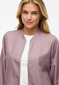 Giubbotto bomber di un delicato colore malva con collo rotondo, zip frontale e tasche laterali, realizzato in tessuto liscio con una leggera lucentezza.