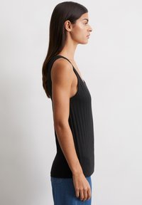 Czarny prążkowany top na ramiączkach o szerokich paskach, dopasowany krój i teksturowany materiał. Noszony z niebieskimi dżinsami, o prostym i eleganckim designie.