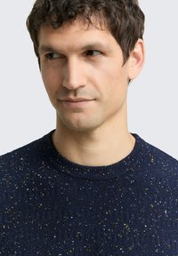 Marineblauer Strickpullover mit strukturiertem Material und mehrfarbigen Einsprengseln, Rundhalsausschnitt und gerippten Abschlüssen. Nahaufnahme des Halsausschnitts und der Schulter.