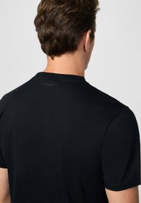 Camiseta negra de manga corta con cuello redondo, hecha de una tela suave. Presenta un sutil logo 'HACKETT' en la parte superior de la espalda.