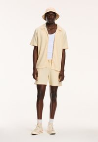Light yellow short-sleeve button-up shirt and shorts made of textured fabric, paired with a matching bucket hat and light sneakers.