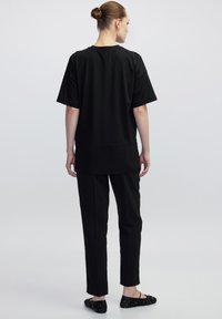 Schwarzes Kurzarmoberteil mit lockerer Passform, kombiniert mit geraden schwarzen Hosen und verzierten schwarzen Ballerinas. Glattes Material und minimalistisches Design.