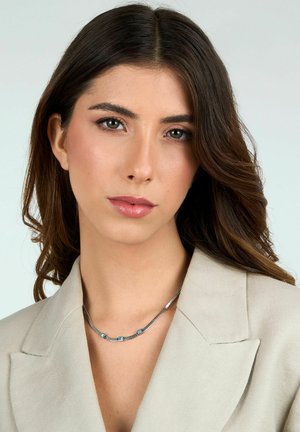 Collana in argento sterling con tre accenti turchesi, caratterizzata da un design elegante e una texture liscia, indossata sopra un blazer beige chiaro.