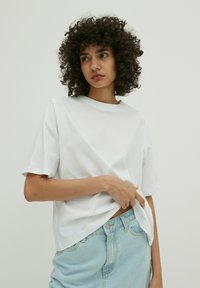 Witte katoenen t-shirt met een relaxte pasvorm, ronde halslijn en korte mouwen, gecombineerd met lichtblauwe spijkerbroek shorts.