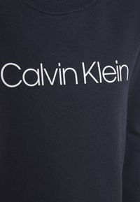 Tessuto blu scuro con il logo bianco "Calvin Klein" stampato sul petto di un capo a collo rotondo.