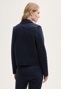 Kornblå kort blazer i texturerat tyg, med spetsig krage och långa ärmar, tillsammans med matchande figursydda byxor.