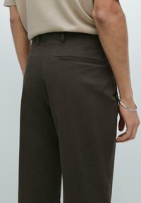 Bruine op maat gemaakte pantalon met een rechte snit, zachte textuur en een achterzak. De tailleband is voorzien van riemlussen voor aanpassingsmogelijkheden.