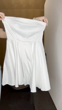 Balta strapless kleita no gludas auduma, ar A formas siluetu un izplešanos svārku, kam ir elastīga bodice, lai nodrošinātu piemērotību.