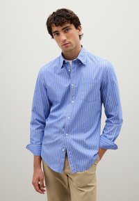 Camicia button-up a righe blu con righe bianche e arancioni, maniche lunghe e taschino sul petto. Tessuto di cotone leggero, vestibilità su misura.
