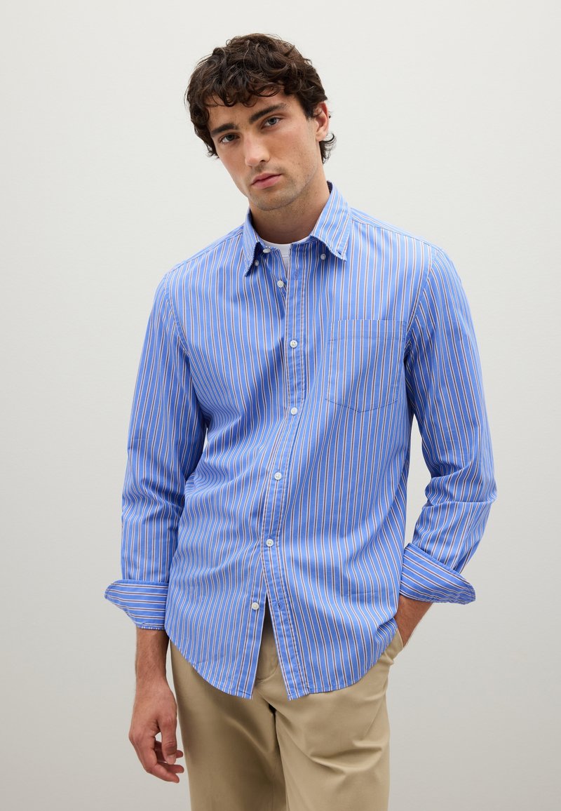 Camicia button-up a righe blu con righe bianche e arancioni, maniche lunghe e taschino sul petto. Tessuto di cotone leggero, vestibilità su misura.
