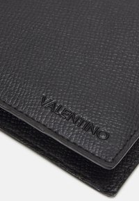 Cartera de cuero negra con un acabado texturizado y el logotipo grabado "VALENTINO". Diseño elegante con bordes limpios y forma compacta.