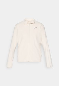 Nike jacket, lightweight, cream color, long sleeves, zip closure, fold-down collar, small black logo on the left chest, smooth fabric texture.