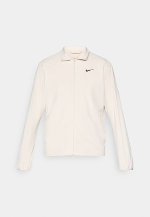 Nike jacket, lightweight, cream color, long sleeves, zip closure, fold-down collar, small black logo on the left chest, smooth fabric texture.