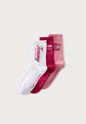 Tre foldede Tommy Hilfiger crew sokker i hvid, mørk pink og lys pink med brandtekstdesign på hvert par.