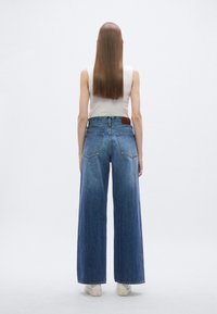 Wijde denim jeans in mid-blauwe wassing, met een hoge taille, vijf zakken en een bruine leren patch op de achterste tailleband. Soepele textuur.