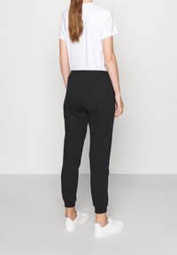 Svarta joggerbyxor med ribbat fåll, elastisk midja och en slät textur, ihop med en enkel vit t-shirt och vita sneakers.