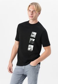 Fekete pamut póló, amelyen három monokróm portré nyomat található az elején, alul "KARL LAGERFELD" felirattal. Rövid ujjú, kerek nyakú.