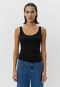 Čierny rebrovaný top s vystrihom a tenkými ramienkami, spárovaný s vysokými modrými džínsy s vreckami na zadnej strane.