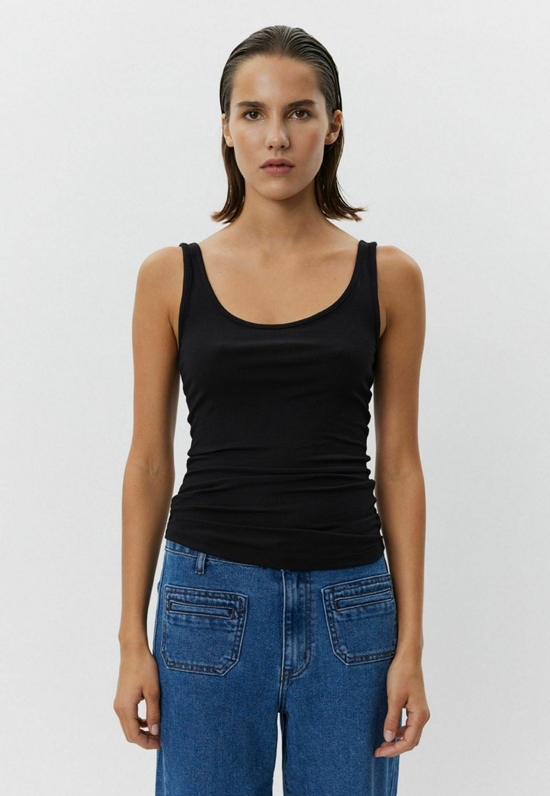 Čierny rebrovaný top s vystrihom a tenkými ramienkami, spárovaný s vysokými modrými džínsy s vreckami na zadnej strane.