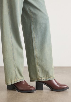 Braune Leder-High-Heels mit quadratischer Zehenform und strukturiertem schwarzen Blockabsatz, kombiniert mit hellblauen weiten Jeans.