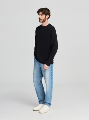 Maglietta nera a maniche lunghe con scollo rotondo, abbinata a jeans azzurri a gamba dritta e sneakers bianche. Design minimalista, trama liscia.