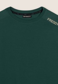 Felpa verde scuro con texture e superficie a coste, dotata di un collo rotondo. Presenta un'etichetta logo di colore chiaro sulla spalla.