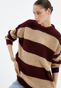 Sweter z dzianiny w poziome bordowe i beżowe pasy, z okrągłym dekoltem, oversize'owym fasonem i prążkowanymi mankietami.
