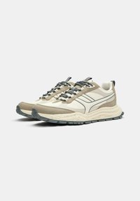 Beżowe buty sportowe z teksturowaną cholewką, szarymi sznurówkami i grubą, cętkowaną podeszwą. Charakteryzują się smukłym designem z kontrastującymi akcentami.